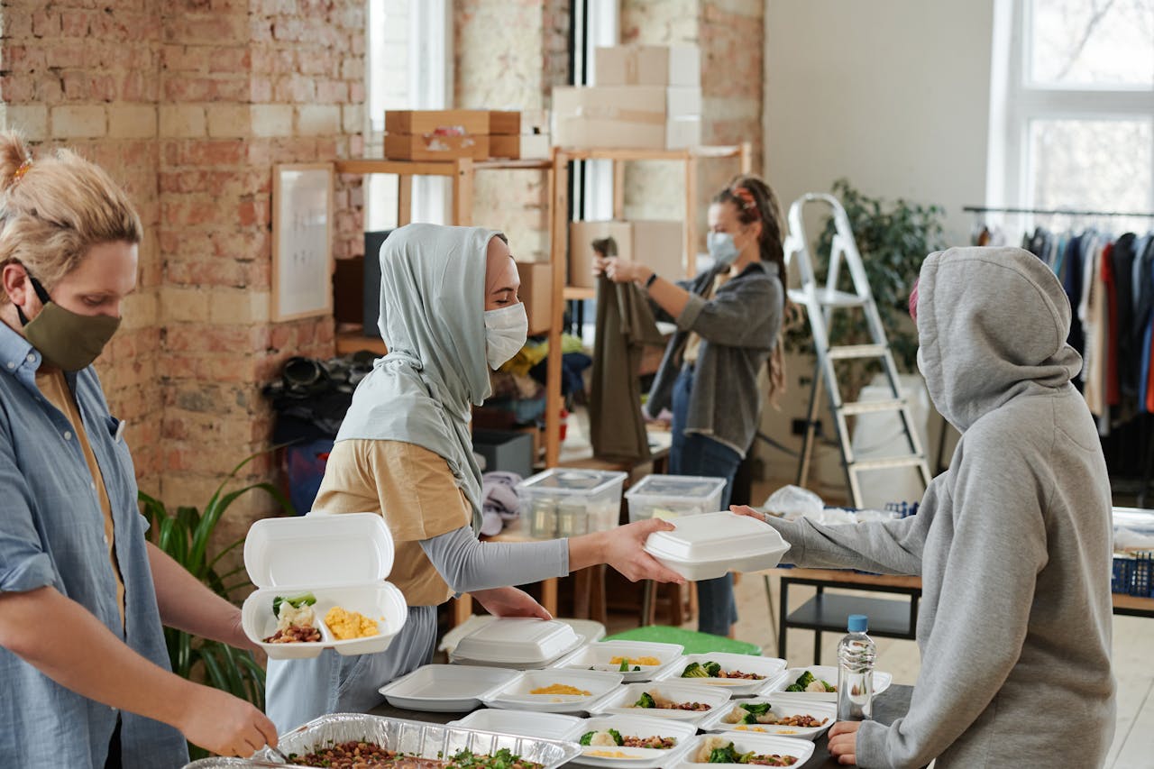 Services Volunteers wearing face masks distribute food in takeaway boxes at a community charity event.