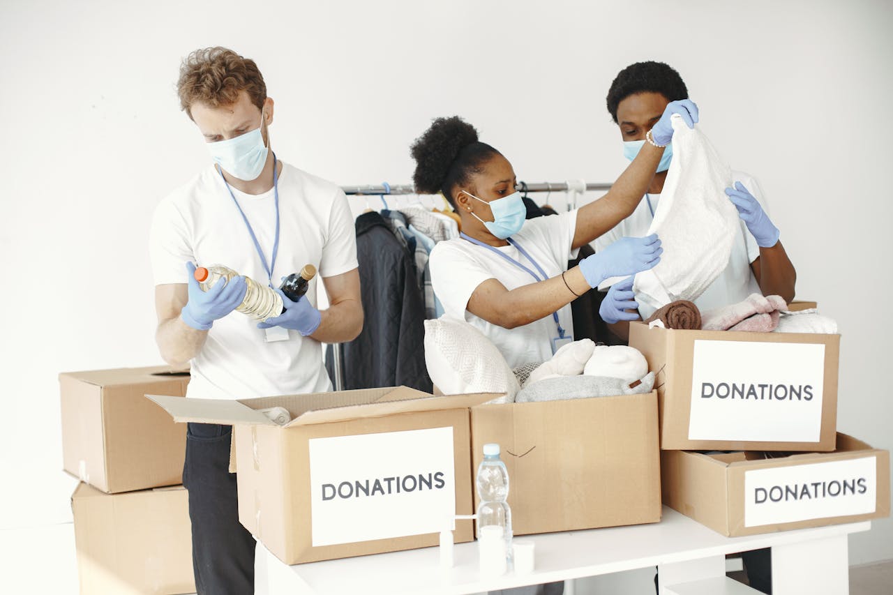 get-in-touch Volunteers wearing masks sort clothes and essentials into donation boxes, promoting charity and safety.