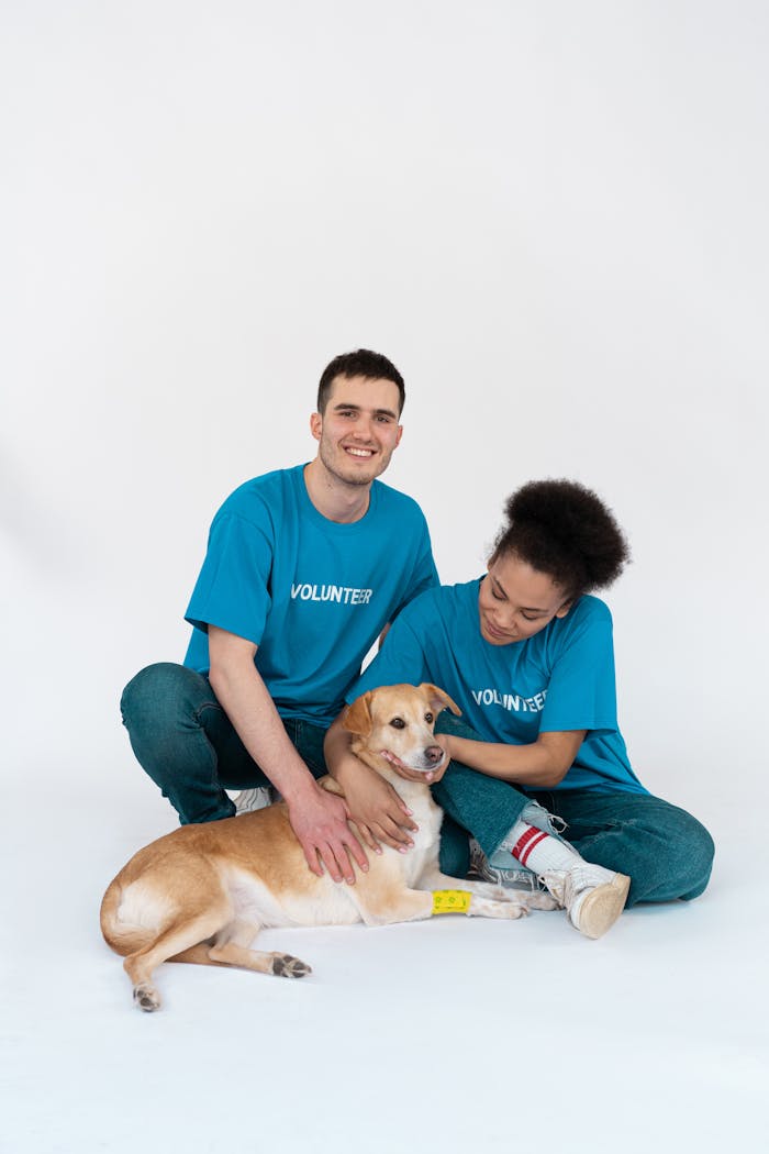 A diverse group of volunteers posing happily with a cute dog in a bright studio setting.